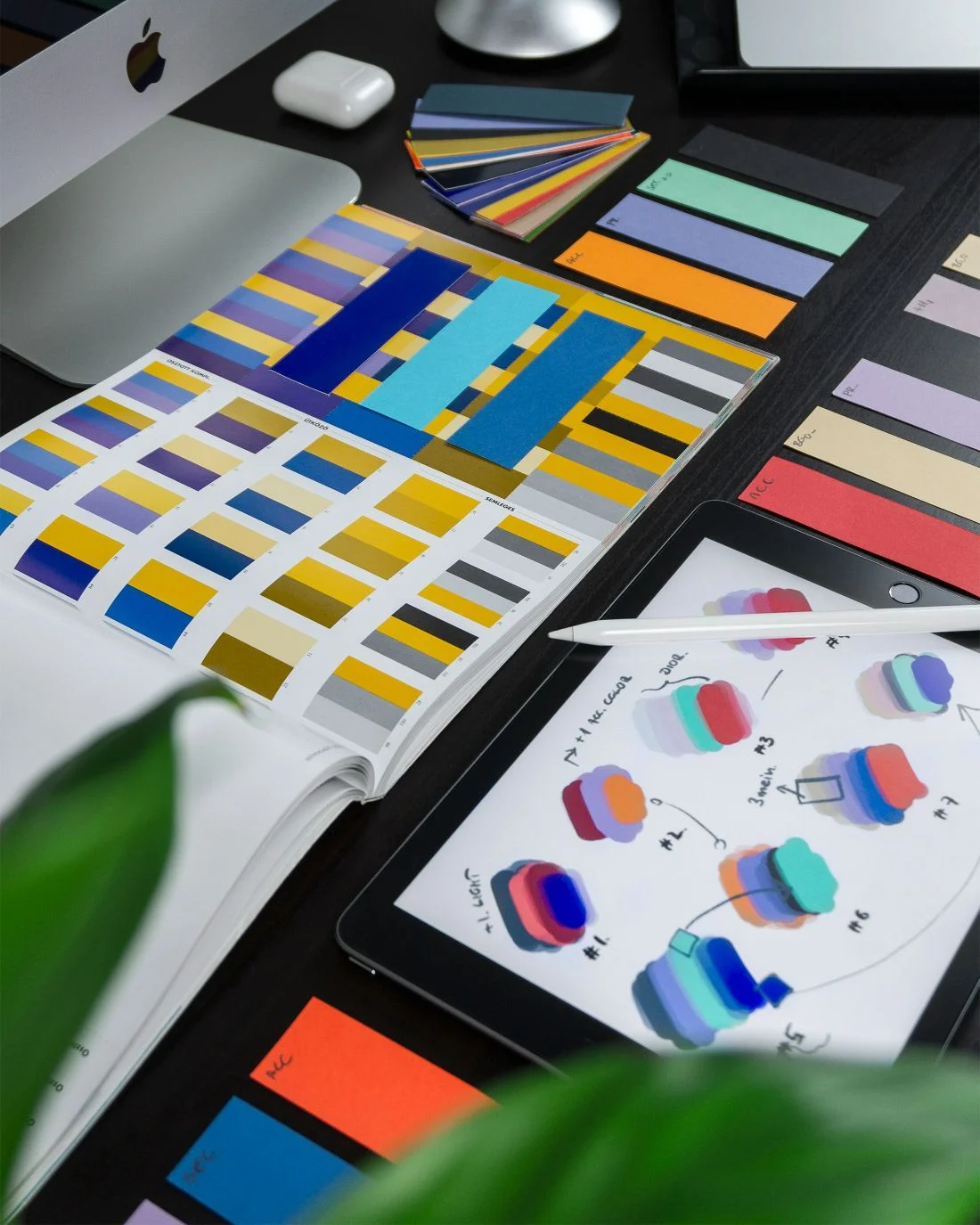 Paper color swatches and a tablet of palette sketches on a dark desk