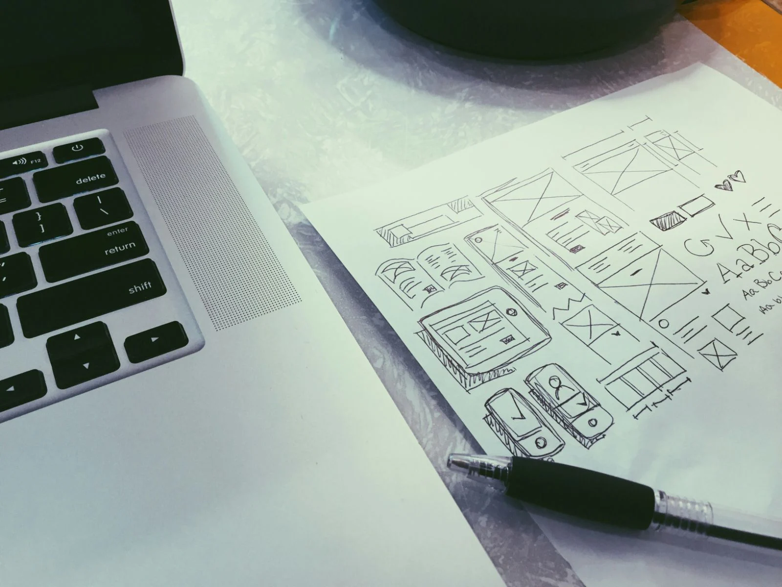 Hand-drawn website wireframe sketches on paper beside a laptop