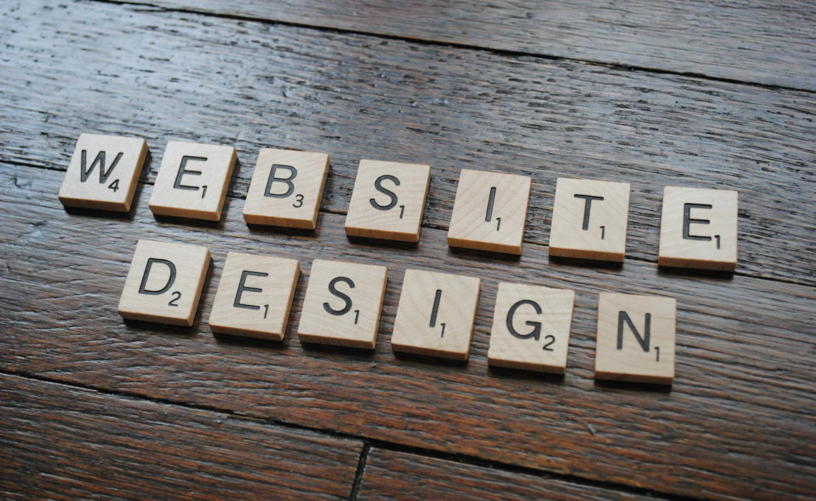 Wooden letter tiles spelling website design on a dark wood table